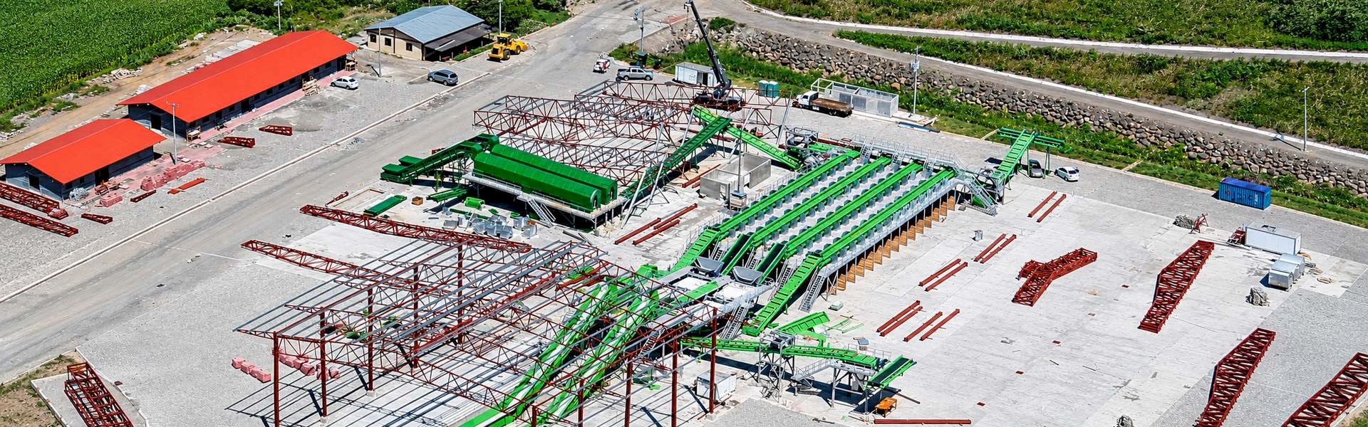 Aerial view of a recycling plant under construction, showing green conveyor systems and structural steel frameworks.
