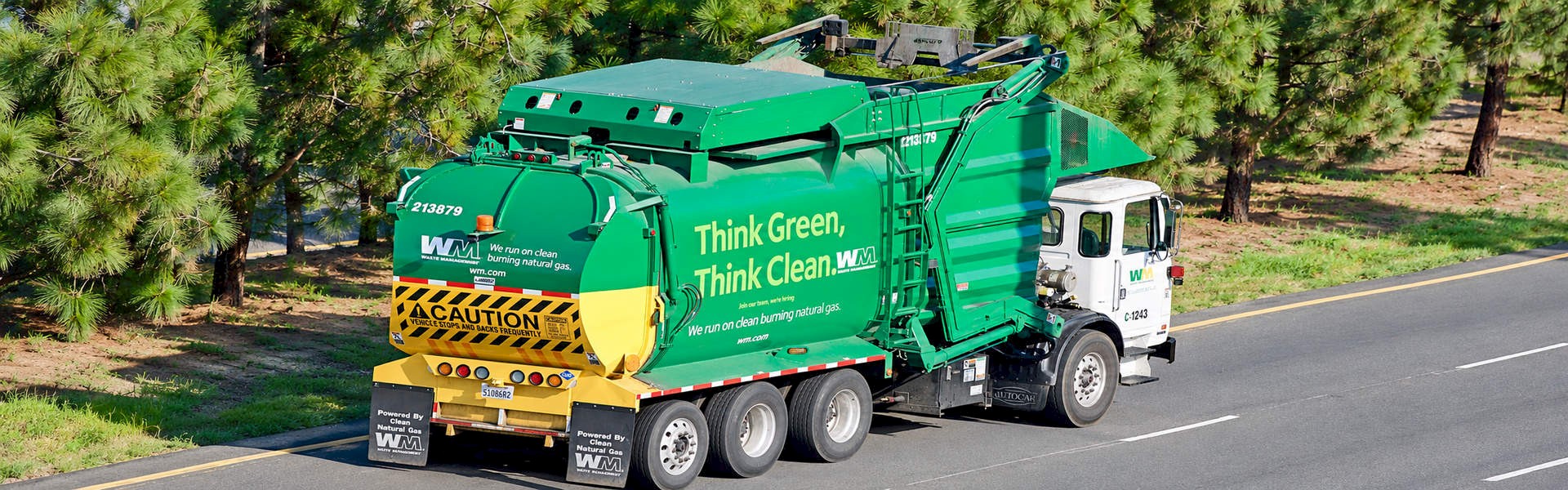 Green waste collection truck travelling along a tree-lined road.