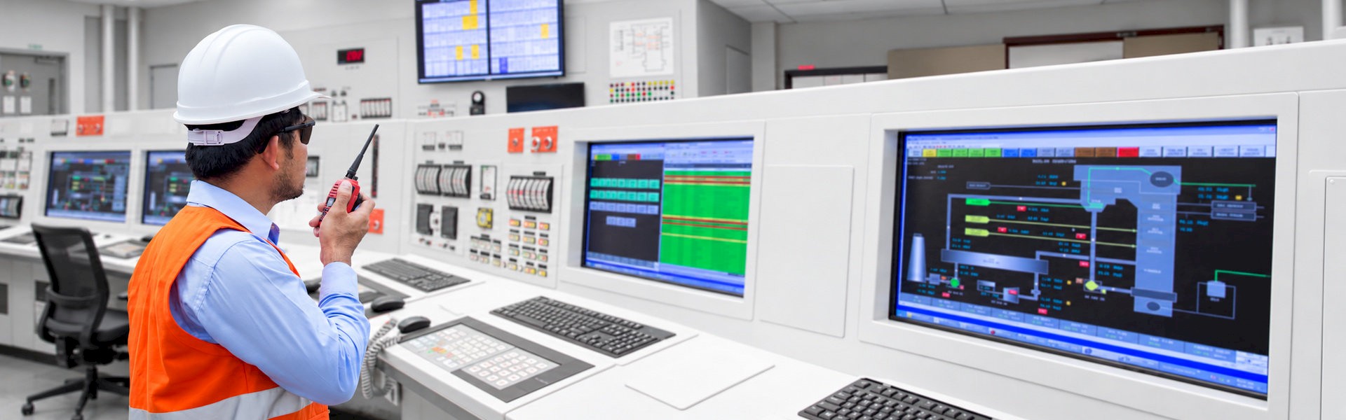 Engineer using a two-way radio while reviewing process monitoring screens in an industrial control room.