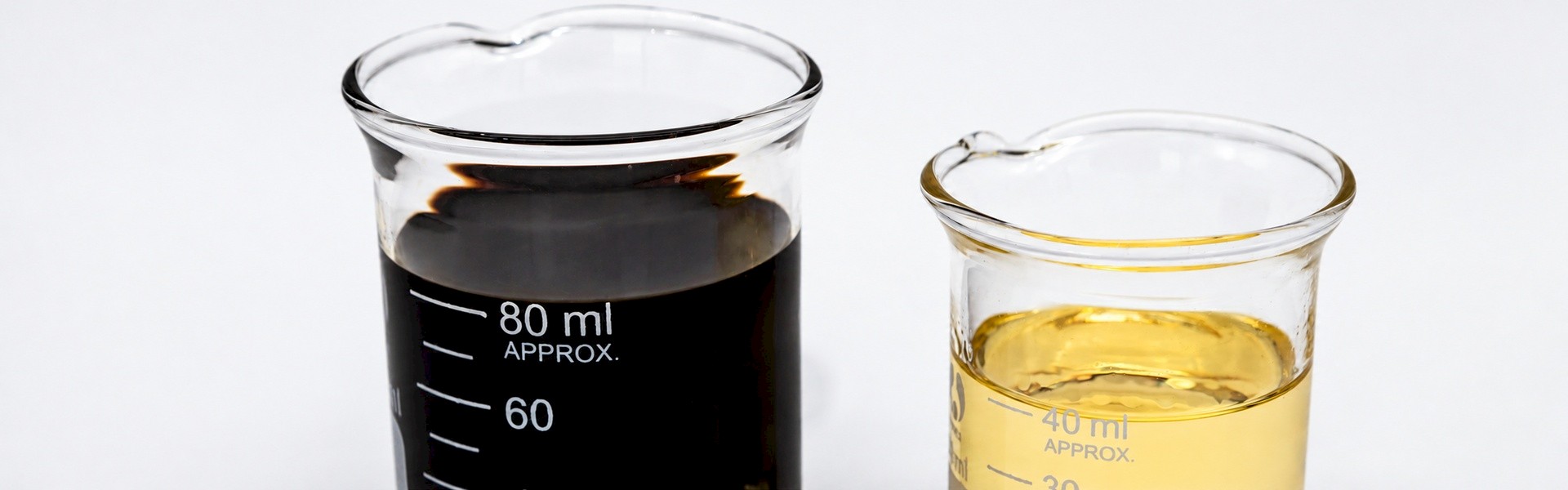 Two glass laboratory beakers containing dark brown and pale golden oil samples.