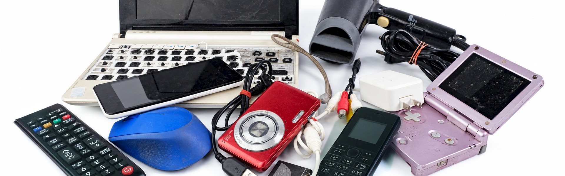 Discarded electronics including a damaged laptop, phones, digital camera, handheld game console, remote control and cables.