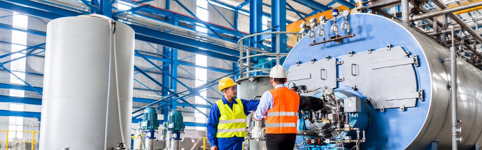 Two engineers inspecting industrial boiler equipment inside an energy plant.