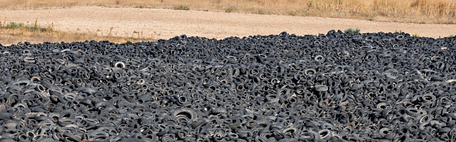 Large outdoor stockpile of scrap tires awaiting recycling, surrounded by dry grassland.