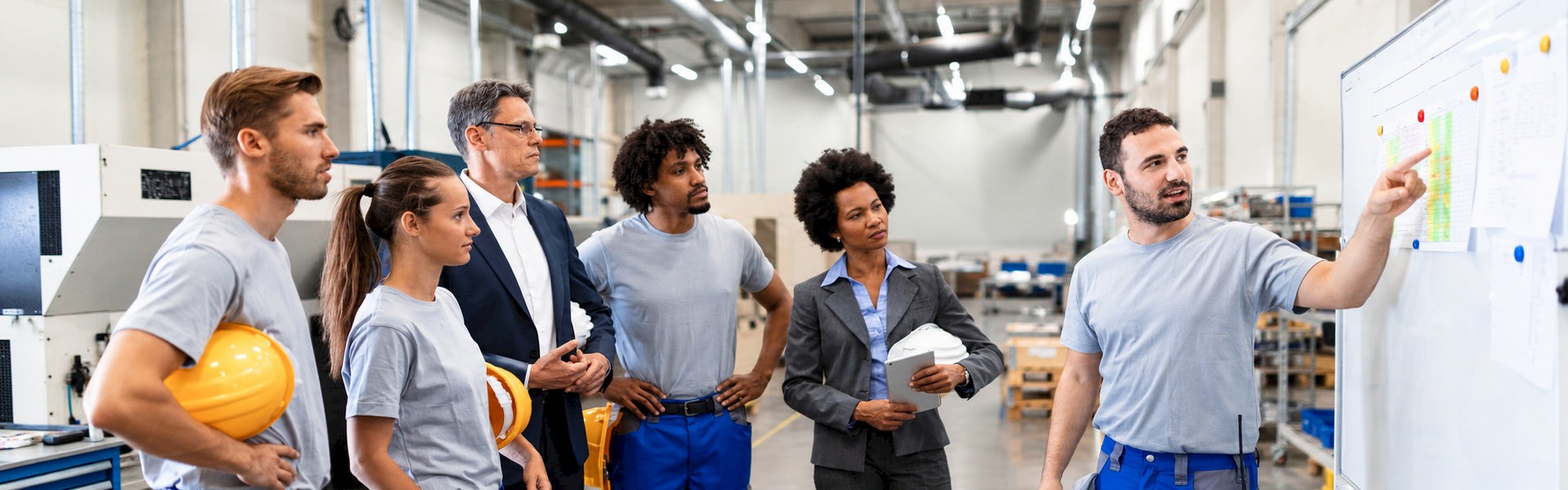 Instructor explaining a whiteboard chart to five attendees during a factory training session.